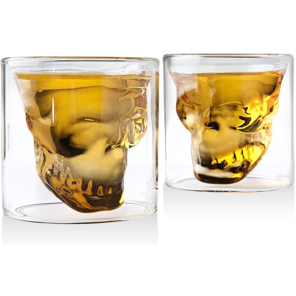 Two skull-shaped glass tumblers filled with whisky a white background