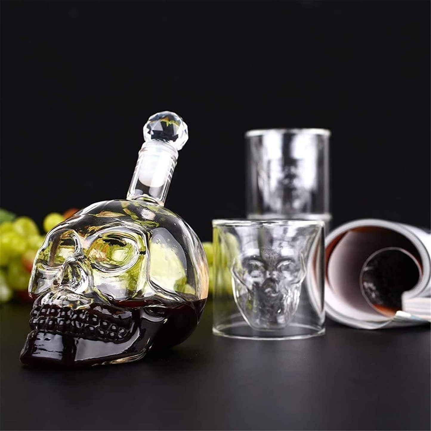 Skull-shaped glass decanter with matching shot glasses on a dark surface.