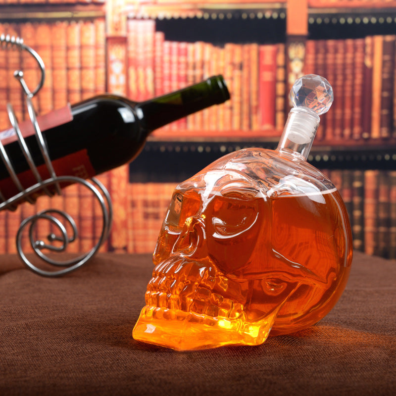 Glass skull decanter with whisky on a brown surface, with a bookshelf in the background.