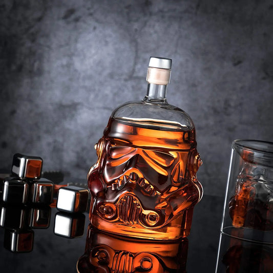 A clear glass decanter shaped like a Storm Trooper helmet from Star Wars, filled with liquid, displayed alongside a glass and metal ice cube.