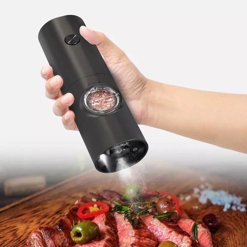 Hand holding a black automatic pepper grinder over a plate of food