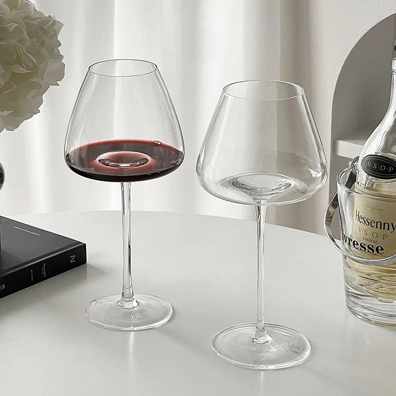 Burgundy crystal wine glasses with red wine on a clean white surface, paired with a bottle in the background for elegant serving and tasting
