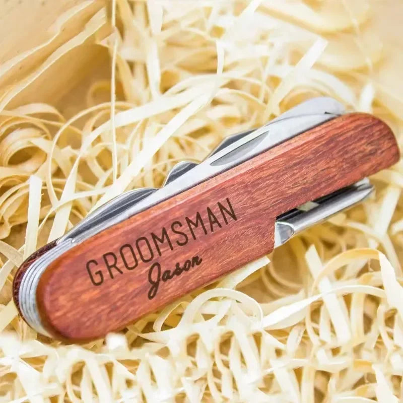 Wooden pocket knife with 'GROOMSMAN Jason' engraving on a bed of straw.