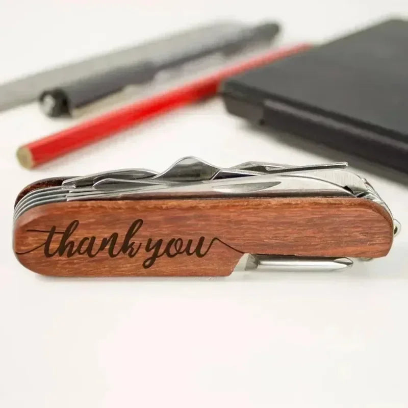 Wooden multi-tool with 'thank you' engraving on a white surface with pens and a notebook.