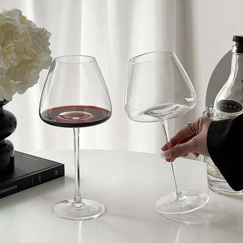 Hand holding Burgundy crystal wine glasses on a white surface, one filled with red wine and one empty, with a softly blurred background for elegant serving and tasting