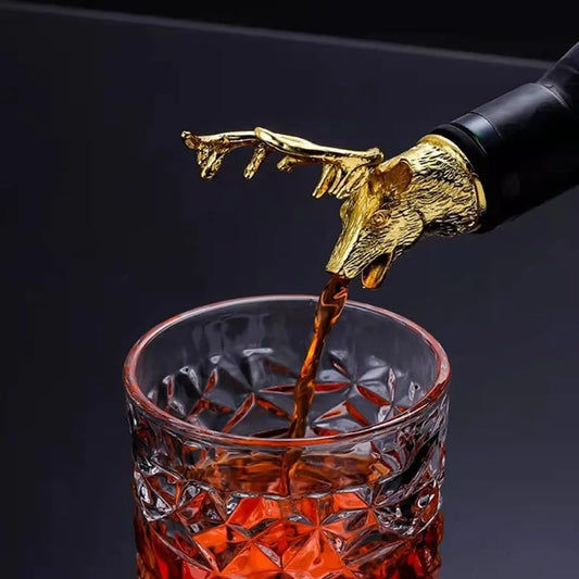 Gold deer head bottle stopper pouring liquid into a glass against a dark background