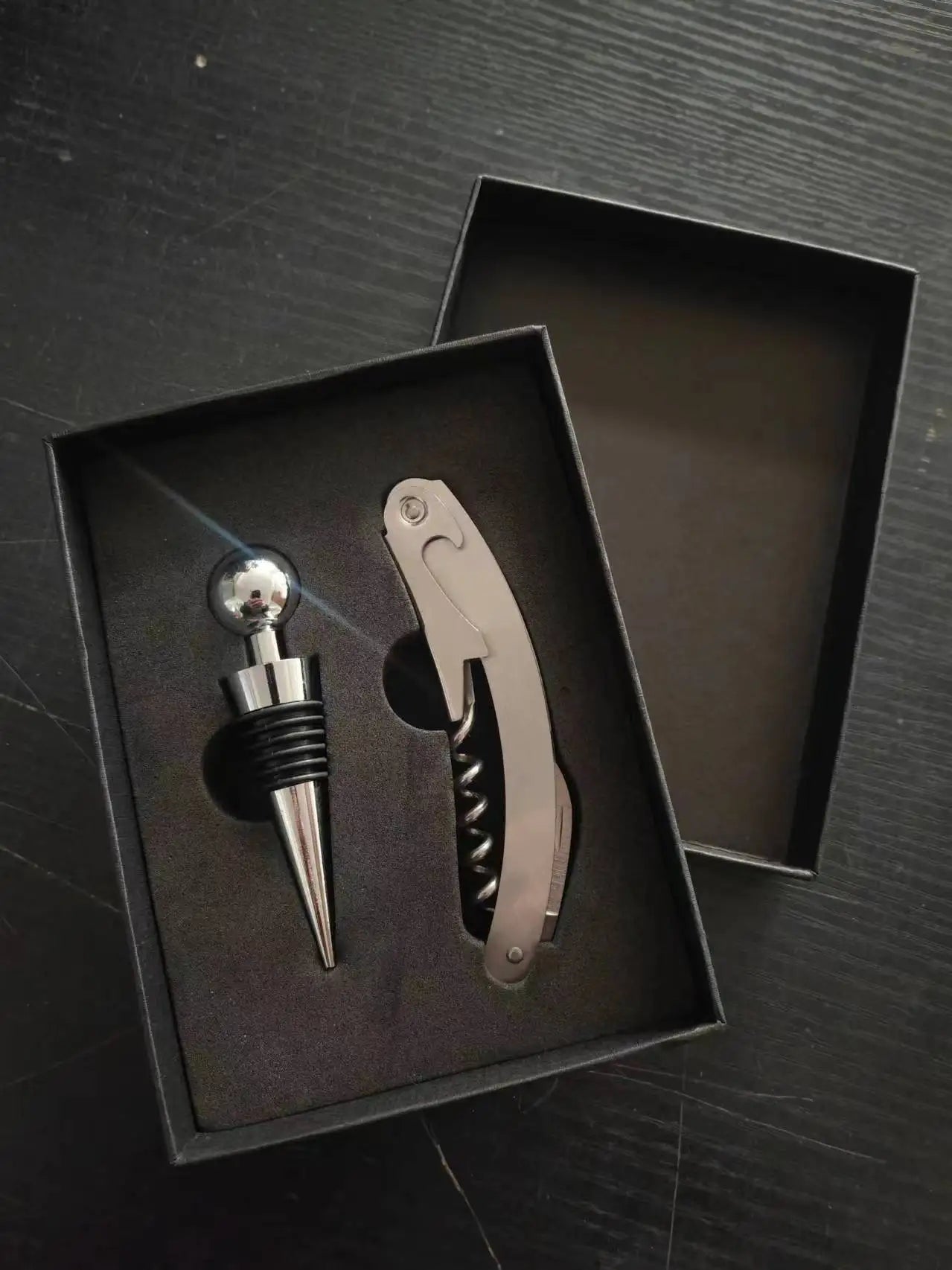 Wine bottle stopper and corkscrew set in a black box on a dark surface