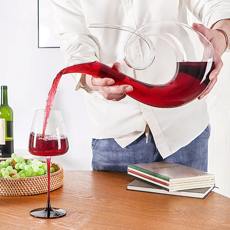 Red wine being poured from wide-base crystal wine decanter into a glass on wooden table for aeration and serving
