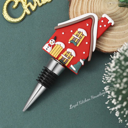 Decorative wine bottle stopper shaped like a red house with snowmen and a ladder on a green background.