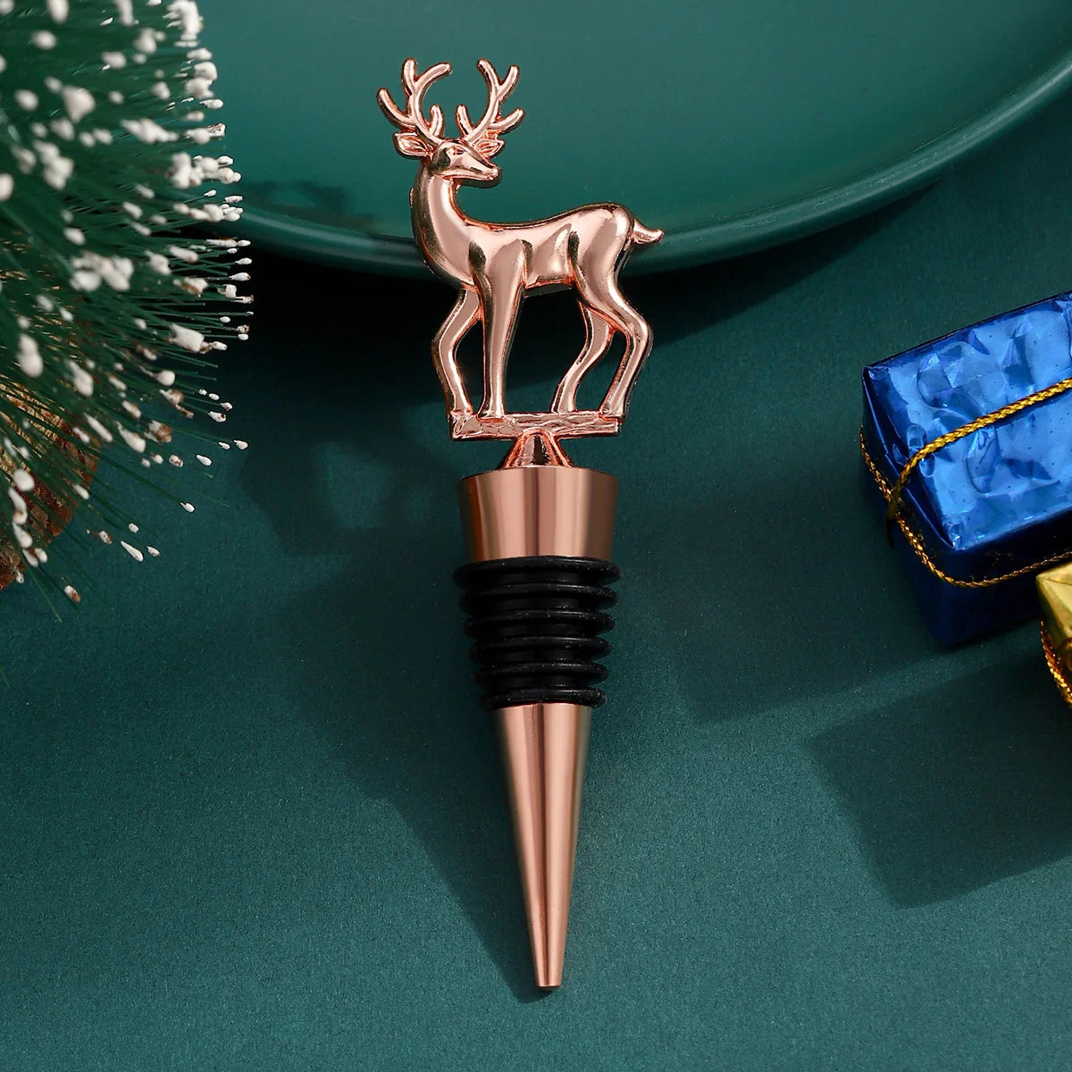 Rose gold deer-shaped bottle stopper on a green surface with a blue gift box.
