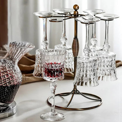 French-style 250ml crystal wine goblets with faceted stem and cut-crystal mounted on a finished metal frame,. A faceted glass decanter and a glass of red wine are partially visible in the foreground and background.

