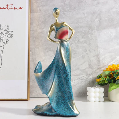 Decorative woman-shaped wine bottle holder in a teal blue dress, displayed on a white surface against a light gray wall.