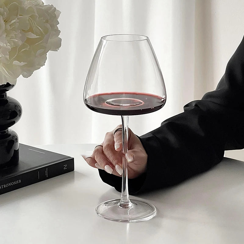 Hand holding a Burgundy crystal wine glass filled with red wine on a white surface with a blurred background for elegant tasting and serving