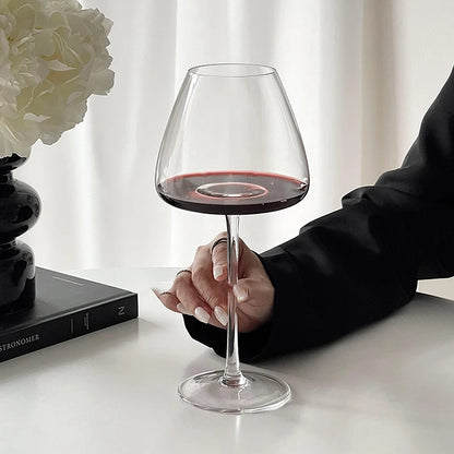Hand holding a Burgundy crystal wine glass filled with red wine on a white surface with a blurred background for elegant tasting and serving
