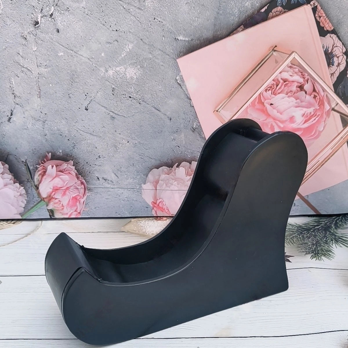 Black wedge-shaped decanter stand on a grey surface with pink floral elements