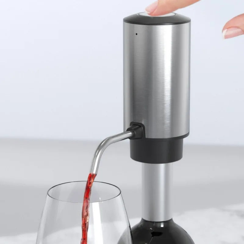 A stainless steel and black electric wine bottle aerator dispenser with a finger pressing the top button, dispensing red wine from a wine bottle into a glass.