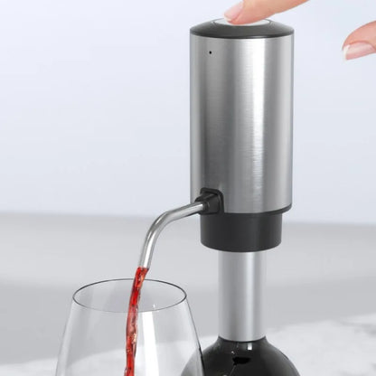 A stainless steel and black electric wine bottle aerator dispenser with a finger pressing the top button, dispensing red wine from a wine bottle into a glass.